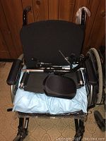 Front view of black fabric manual wheelchair with padded armrests and a blue cushion on plastic wrap