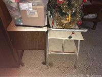 Photo of vintage aluminum rolling table with white surface showing wear and stains, next to storage bin and wooden furniture