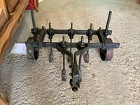 Front view of antique metal garden cultivator showing 2 wheels and 4 cultivating tines on a metal frame.