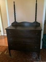 Front view of antique wooden dresser showing three drawers, two turned wooden posts and overall dark stained wood surface.