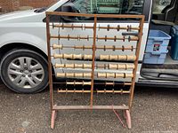 Front view of antique wooden spool rack showing various sizes of wooden spools, some holding thread, with a white vehicle door in background.