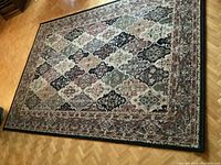 Full view of the rectangular carpet laid flat on a wooden parquet floor showing entire pattern and border.