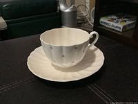 Cup and saucer set shown on a dark surface with surrounding room elements visible. Shows the front and top view highlighting star patterns and handle.