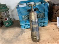 Small brass fire extinguisher on a wooden surface next to a blue plastic crate and a green lantern.