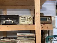 Three vintage radios placed on a wooden shelf; a black Motorola radio, a cream-colored radio, and a wooden cabinet radio