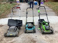 Three lawnmowers side by side on a driveway showing two electric and one battery-operated mower with grass bags