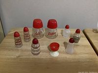 Full view of nine pieces: three sets of vintage glass salt and pepper shakers with red tops, two single salt shakers, and one red-topped egg cup