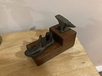 Cast iron shoe form and miniature anvil mounted on oak stand against a wall, showing overall lot presentation.