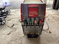 Front view of vintage Coca-Cola fountain dispenser showing 4 dispensing levers and beverage lines attached.