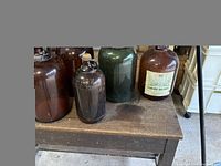 Photo showing five vintage wine bottles on a wooden bench, including the green bottle and the Javex bottle.