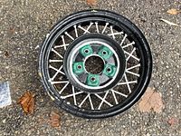 Top view of vintage painted wire spoke car rim showing black outer rim, white metal spokes, and green center hub with bolt holes.