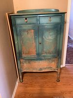 Full view of the vintage tall dresser showing front, two small top drawers, doors and distress of paint.