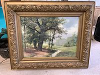 Overall photo of framed watercolor painting depicting a forested creek landscape in a detailed vintage gold frame.