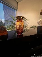 Photo of a vintage glass vase on a polished black surface with a window in background showing outside buildings and plants.