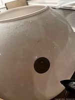 Close-up photo showing the pearl-colored glass vase with a Cambridge maker's mark sticker affixed to the surface, confirming its origin.