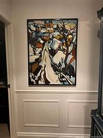 Full view of the framed signed artwork depicting a stylized snow-covered village scene hung on a wall