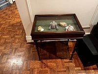 Front view of the vintage wooden display table with glass top showing interior and turned legs on wood floor.