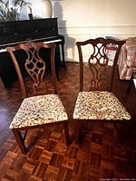 Two vintage wooden chairs with carved backs and brown/beige patterned upholstery shown against a parquet floor and near a piano.