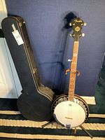 Full view showing Fender banjo on stand next to hard shell case
