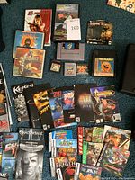 Multiple cartridges, VHS and PC game manuals arranged on blue carpet