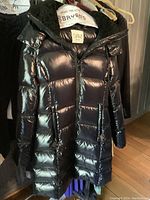 Black Sam New York full-length puffer coat hanging on rack