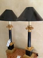Front view of both lamps on marble-top table showing black shades and gold accents