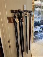 Five belts hanging on wooden rack, showing full-length straps and buckles