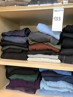 Two shelves holding seven folded sweaters on top shelf and five on bottom shelf, assorted dark and light colors
