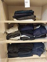 Three-shelf cabinet with folded denim jeans on top shelf and folded shirts on middle and bottom shelves