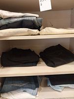 Four pairs folded on top shelf: cream, grey striped, black and beige trousers