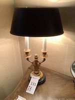 Front view of one lamp showing dual candle‐style bulbs, gilt metal body, marble base and black shade