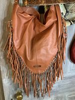 View of a tan fringed leather purse with chain details and soft slouchy structure