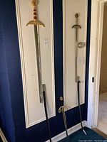 Three swords displayed against wall and leaning on floor showing overall lot
