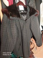 Photo of a black quilted coat with a fur collar hanging on a hanger.