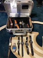 Silver humidor carrying case open showing multiple watches inside and arranged on black watch rolls