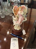 Angel figurine with pink wings, floral base on a wooden music box, with handwritten tag 'Angel with Heart' and a pen for size reference.
