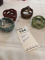 Four beaded wrap bracelets in blue, red, brown, and green colors on a white lace cloth background with a Maxsold lot card showing lot number 534.
