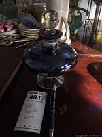 Blue glass decanter with stopper standing on a wooden surface, reflecting light showing shiny finish.