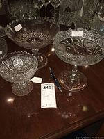 Three clear glass stemmed compotes on a dark wood surface, showing detailed pressed glass patterns.