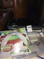 Photo showing FoodSaver Plus vacuum sealer machine with attached hose and nozzle, partially obscured by boxes and bags.