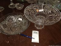 Pedestal fruit bowl and seven matching crystal-style glass fruit bowls on a wooden surface with pen and auction tag