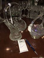 Large glass basket with curved handle and diamond cut body alongside the smaller basket