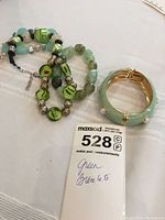 Three green bracelets including the gold-tone enamel bangle and two beaded bracelets with varying shades of green beads.