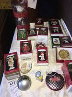 Photo showing multiple boxed Hallmark Keepsake Christmas ornaments including character figurines and thematic designs, plus unboxed small metallic and multicolored egg ornaments on a white surface.