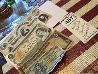 Photo showing Canada One Dollar bill, Confederate currency, and US Allied Forces Five Cents note laid out on a surface with a handwritten lot tag.