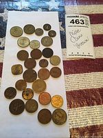 Coins of various sizes and denominations arranged on a white rectangular cloth with a MaxSold lot label beside them showing lot number 463 and description "Misc Coins Bronze".