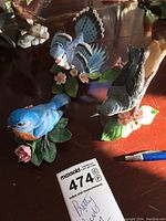 Three blue ceramic bird figurines by Lenox displayed on a wooden table with natural lighting. Shows detail on bird wings, feathers, and flower bases.