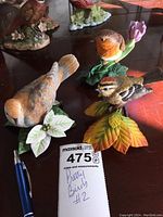 Three yellow toned bird figurines displayed on brown table surface with pen for scale and note card reading 'Pretty Birds #2' handwritten