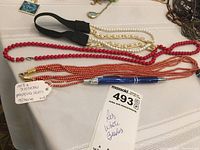 Photo of three necklaces arranged on a table with a pen and a lot tag labeled 'Red White Beaded Necklaces'.