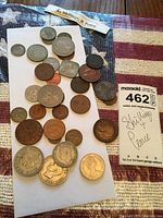 Various vintage coins scattered on white paper with a USA flag patterned fabric background, includes multiple shillings and pence coins of different sizes and designs.